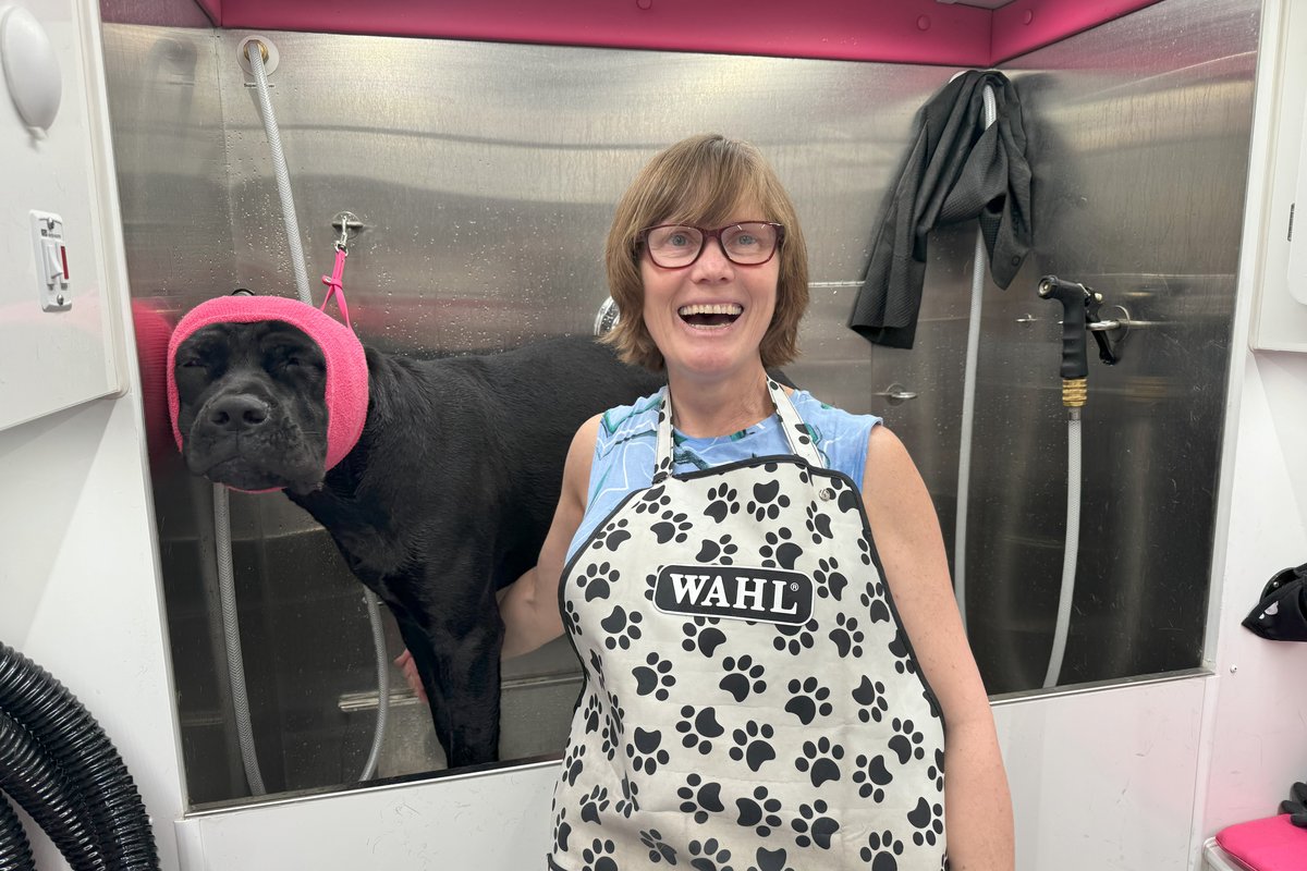 Helen laughing with a black lab in the grooming tub inside the Bow Tie mobile salon