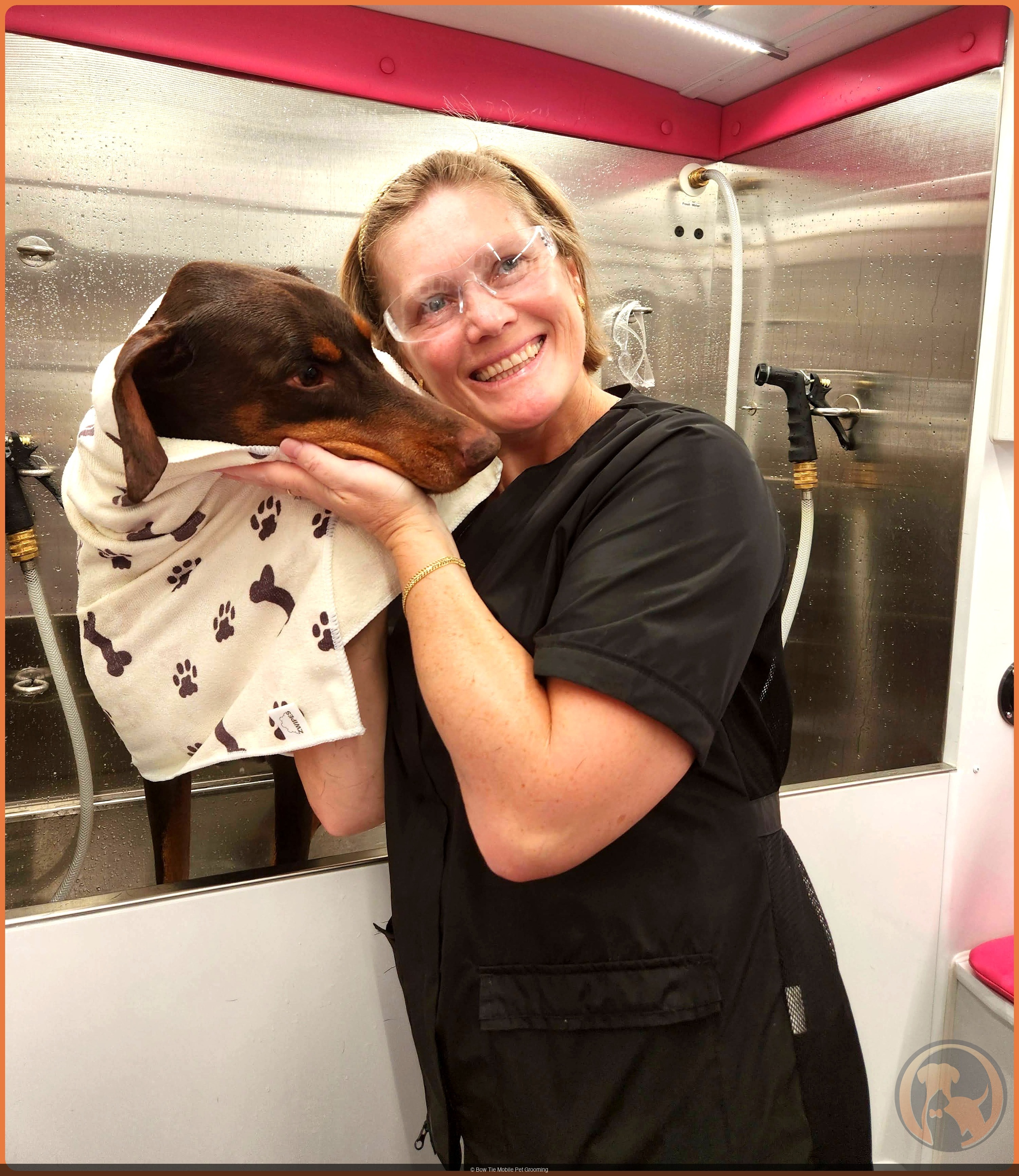 Helen cradling a Doberman wrapped in a paw-print towel after a bath inside the Bow Tie mobile grooming van